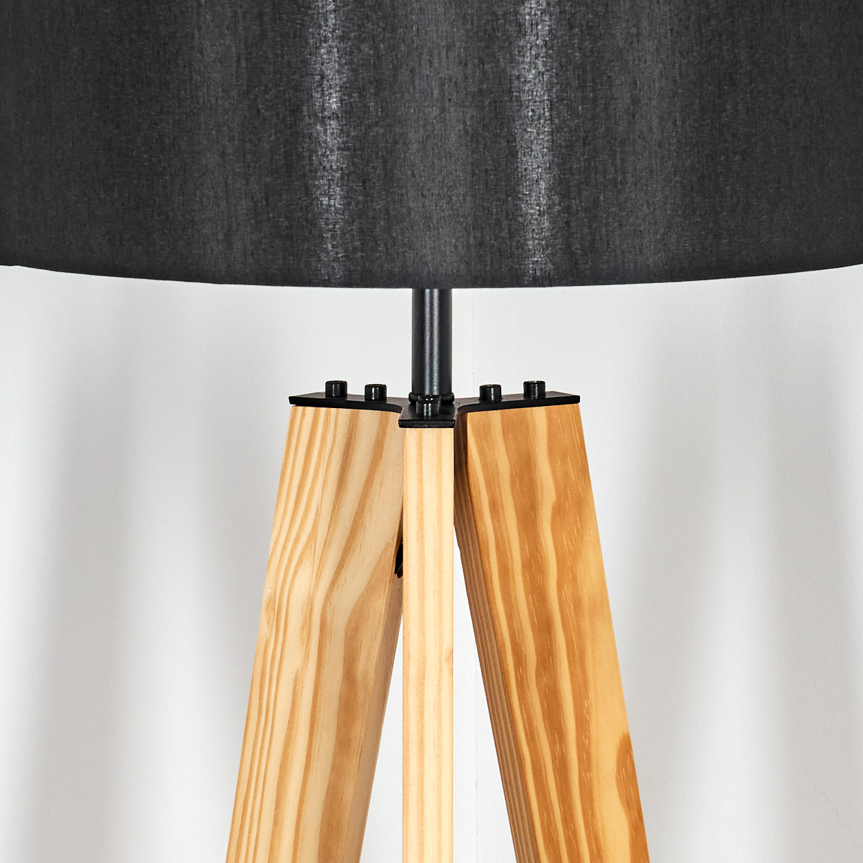 Nahaufnahme einer Stehlampe. Sie hat einen schwarzen Lampenschirm und Holzbeine. Der Hintergrund ist eine schlichte weiße Wand.
