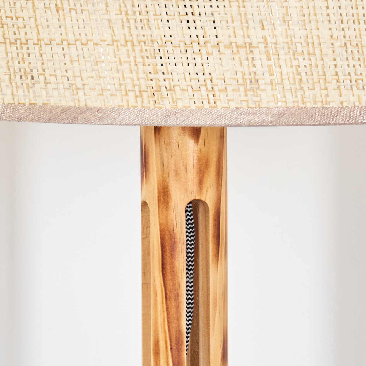 Nahaufnahme einer Lampe. Beiger gewebter Lampenschirm über einem Holzpfosten mit einem schwarz-weißen Zickzack-Kabel. Weißer Hintergrund.