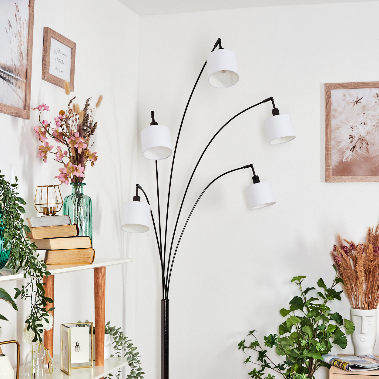 Modernes Wohnzimmer mit schwarzer Bogenlampe, weißen Lampenschirmen und Deko wie Blumen, Büchern und Pflanzen.