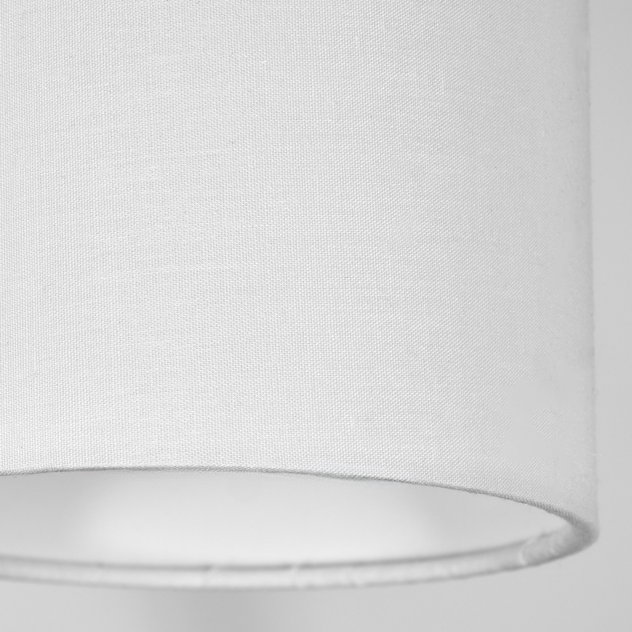 Nahaufnahme eines weißen Lampenschirms. Der Stoff ist strukturiert. Der Hintergrund ist ein schlichtes, helles Grau.