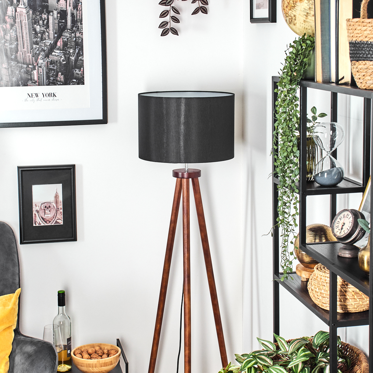 Ein Raum mit einer hölzernen Stativlampe, einem schwarzen Lampenschirm, einem Regal mit Dekorationen und einem New York-Poster an der Wand.