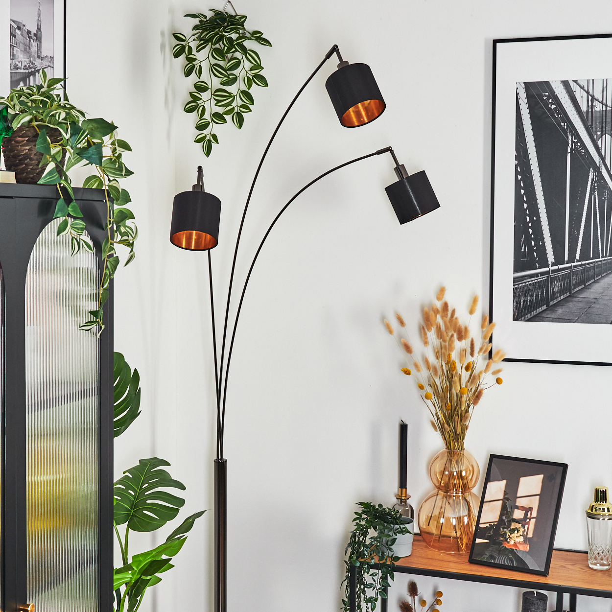 Ein modernes Wohnzimmer mit schwarzer Stehlampe, Pflanzen, Brückenfoto im Rahmen und Dekoration auf Holzregal.