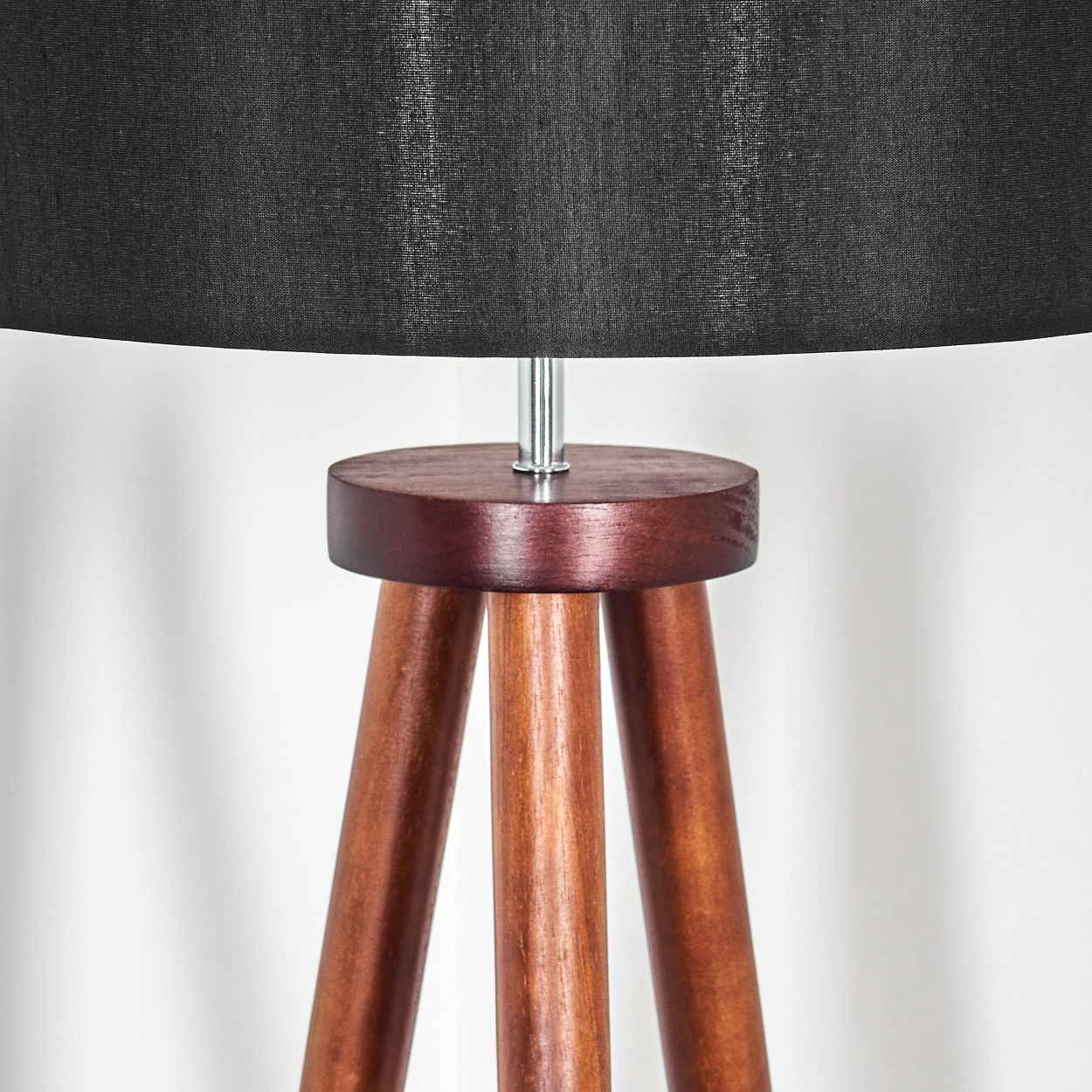 Nahaufnahme einer Holz-Dreibein-Lampe mit schwarzem Lampenschirm. Die Lampe hat einen dunkelbraunen Holzfuß und eine silberne Stange.