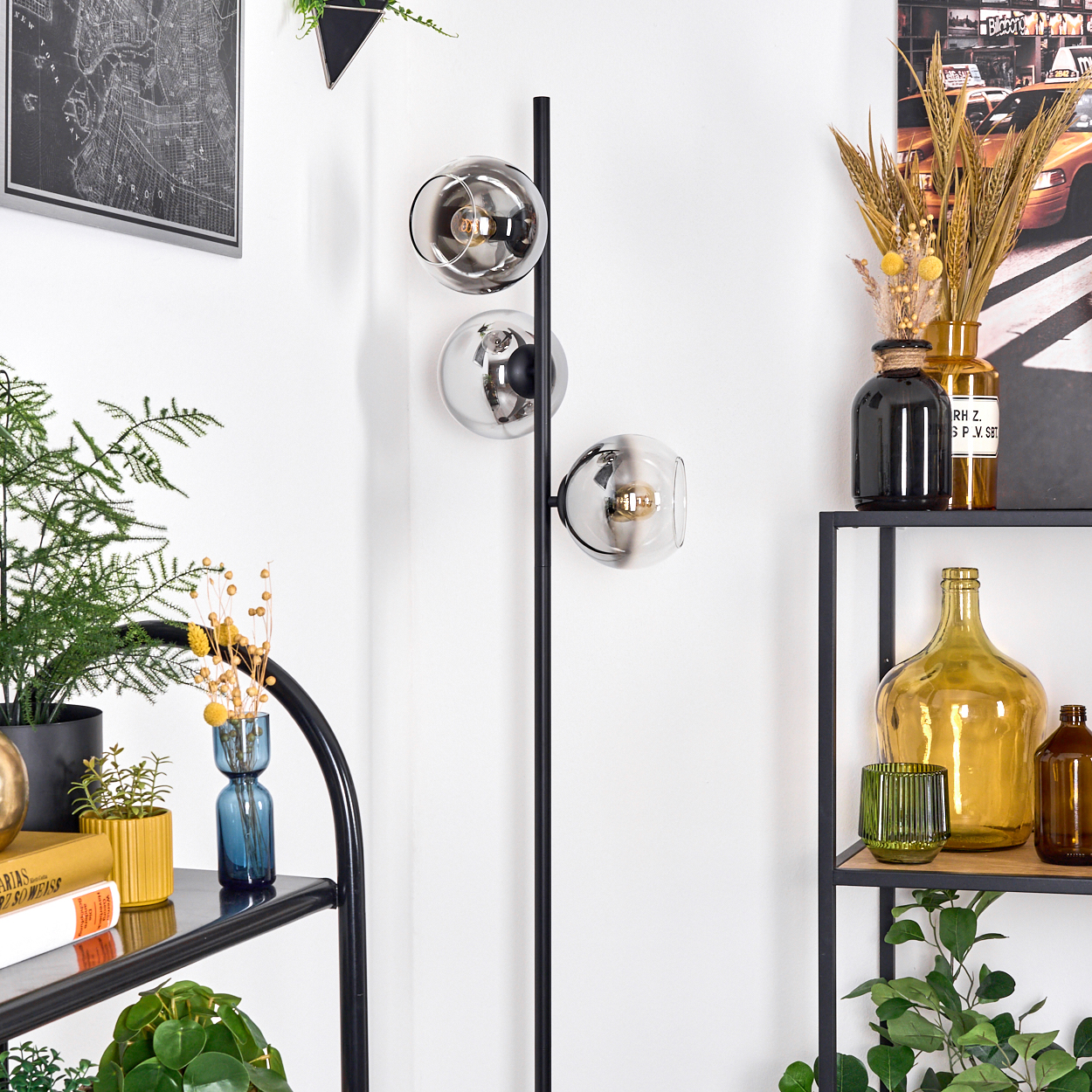 Eine moderne Stehlampe mit Glaskugelschirmen steht neben einem Regal mit Vasen und Pflanzen. Eine Karte und Dekoration befinden sich im Hintergrund.
