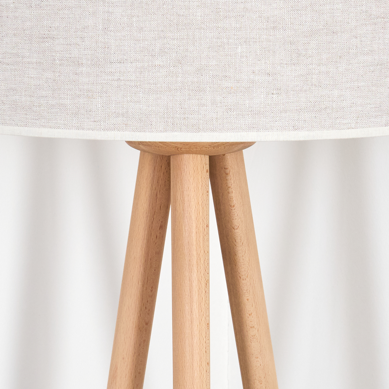 Nahaufnahme einer Holz-Stativlampe. Ein beiger Lampenschirm sitzt auf den drei Holzbeinen vor weißem Hintergrund.