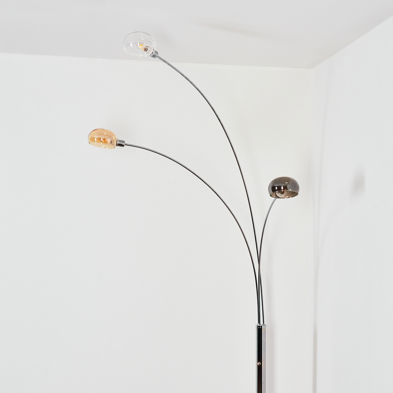 Eine moderne Stehlampe mit drei gebogenen Armen, die jeweils ein rundes Licht halten. Die Lichter sind verschiedenfarbig, vor einer weißen Wand.