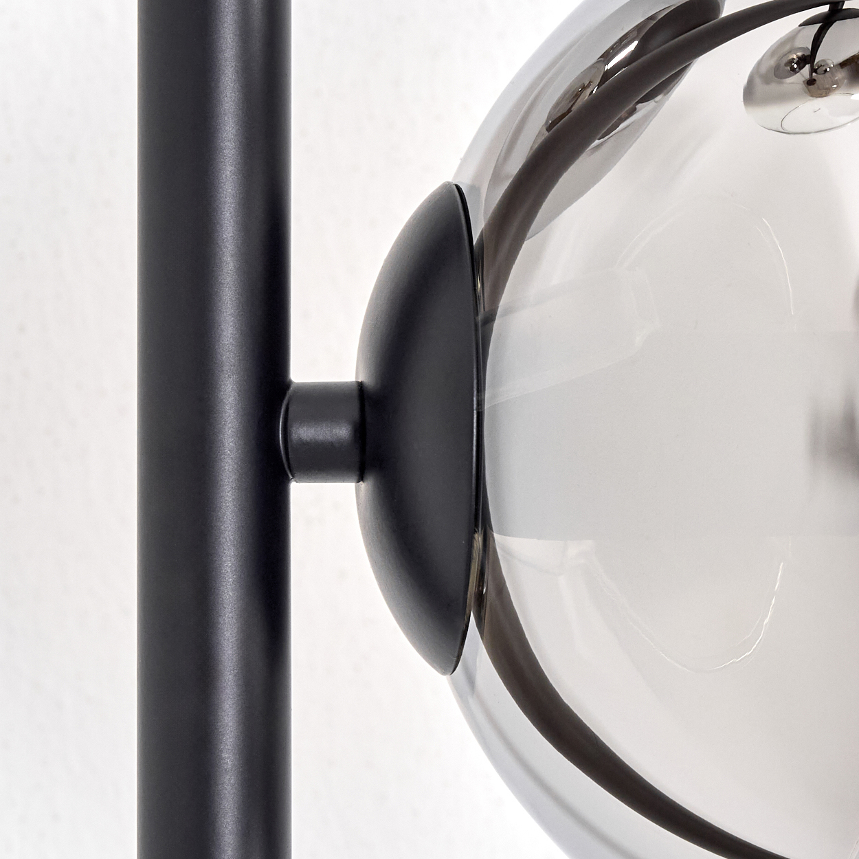 Nahaufnahme einer modernen Lampe. Sie hat einen schwarzen Pfosten und eine klare Glaskugel mit interner Verkabelung. Der Hintergrund ist weiß.