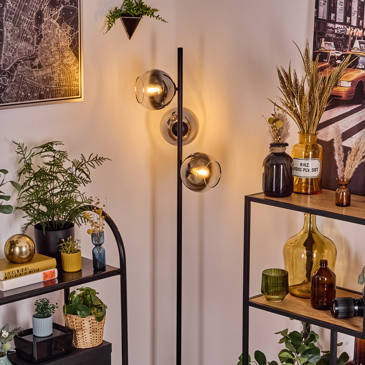 Eine Zimmerecke mit Stehlampe, Regalen mit Pflanzen und Vasen, sowie einer Karte und einem Stadtbild an den Wänden.