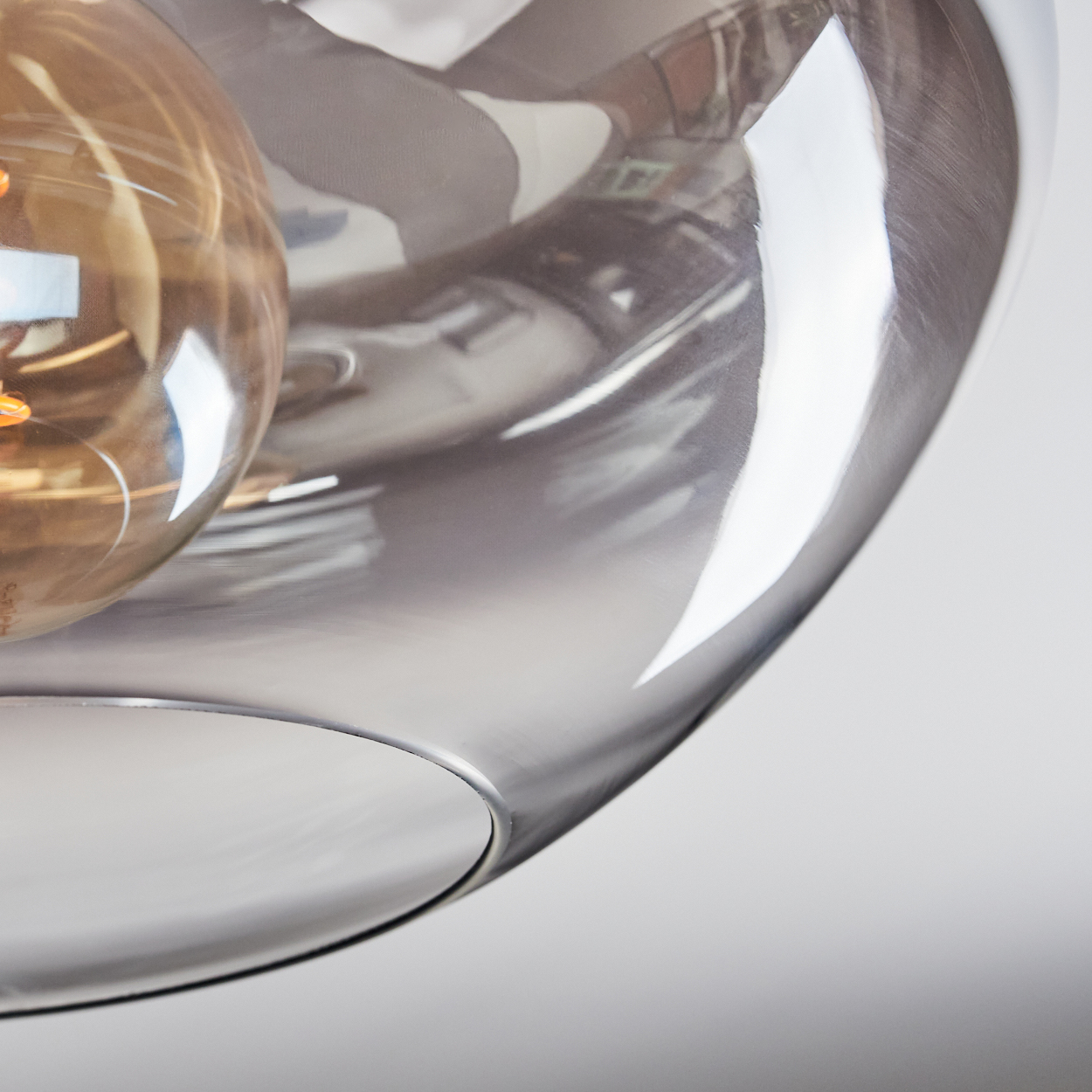 Nahaufnahme eines Glasschirms mit einer Glühbirne. Das Glas ist transparent und reflektiert die Umgebung.