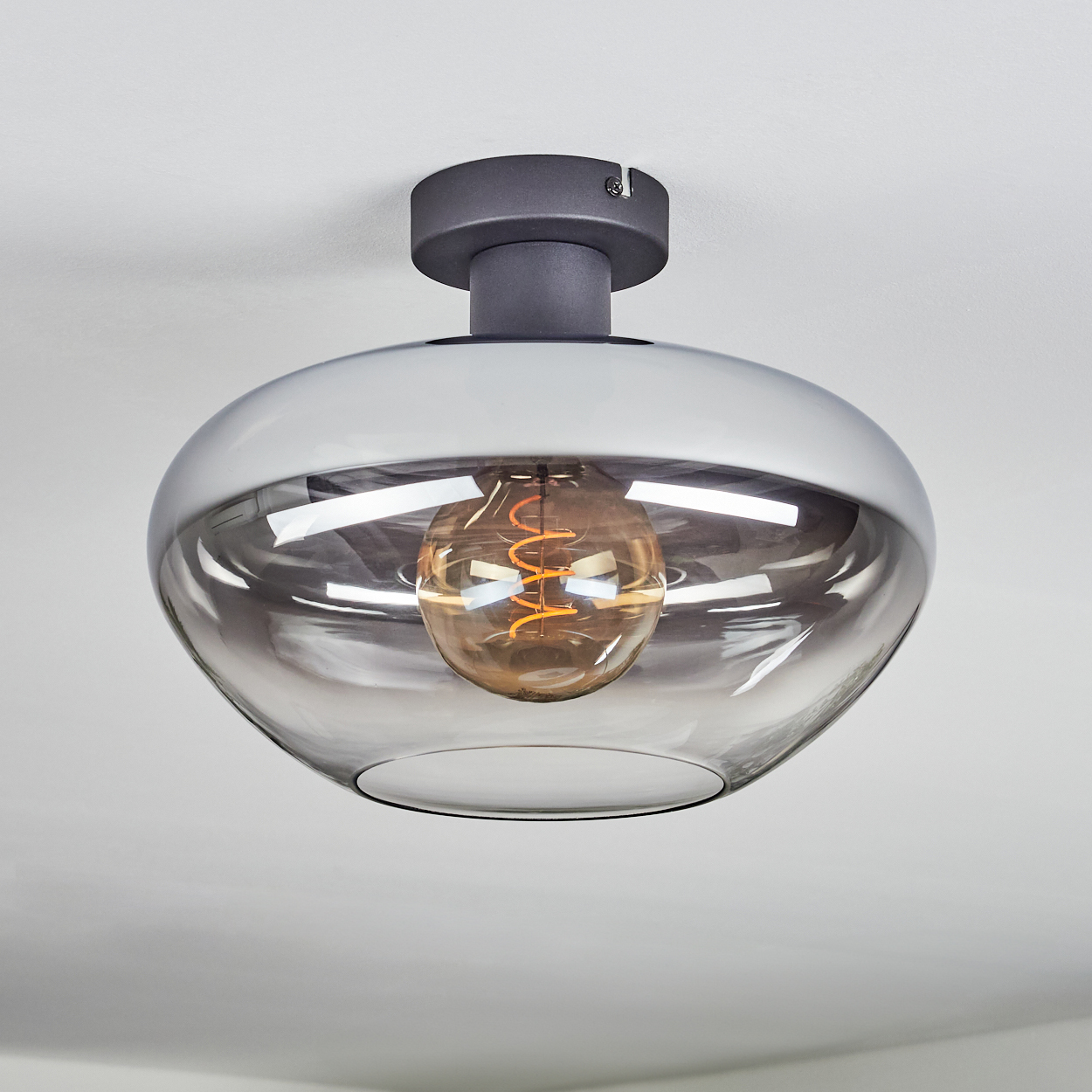 Eine moderne Deckenleuchte mit rauchfarbenem Glasschirm und einer warm glühenden Glühbirne.