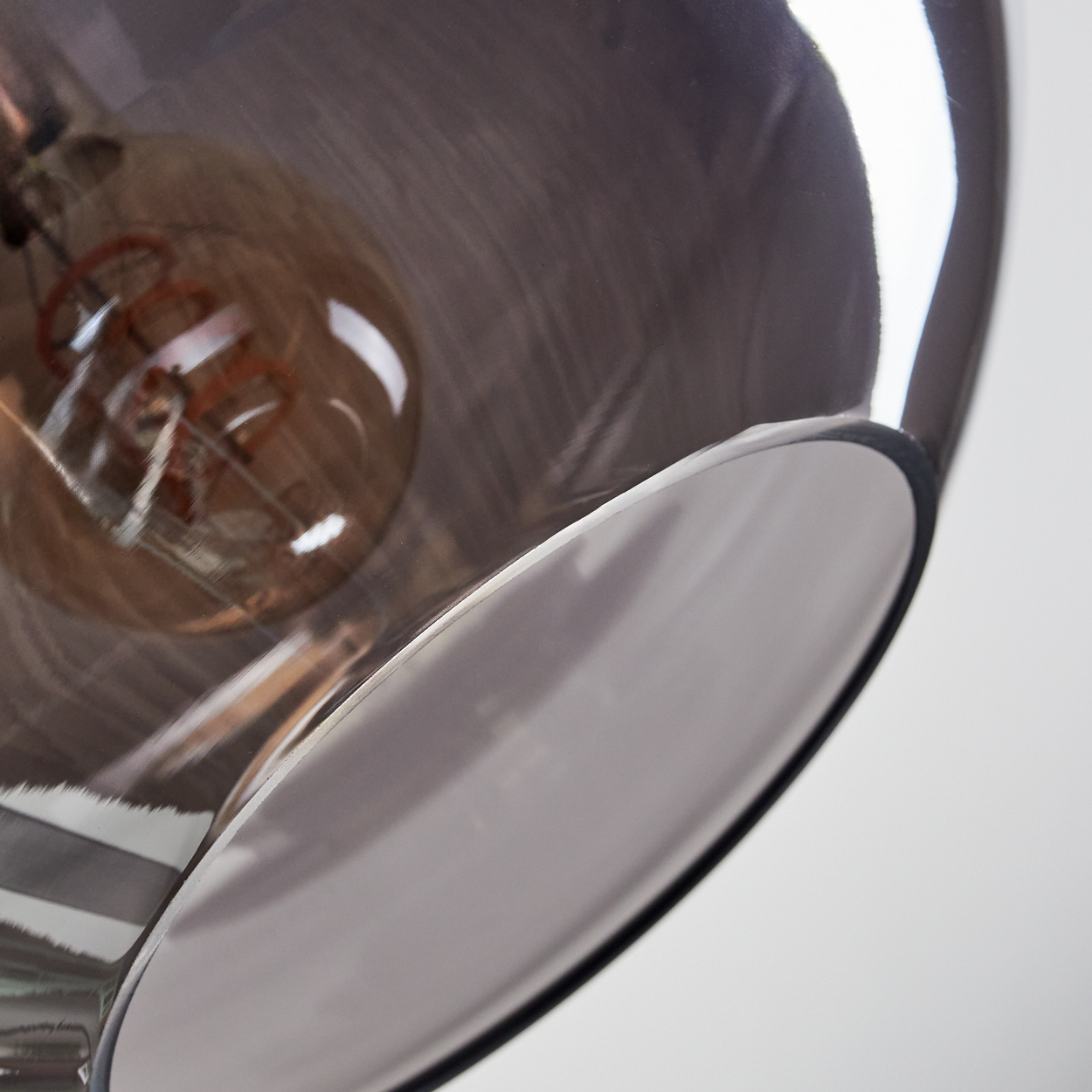 Nahaufnahme einer Lampe. Der Schirm ist grau und reflektierend. Im Inneren ist eine Glühbirne zu sehen. Der Hintergrund ist weiß.