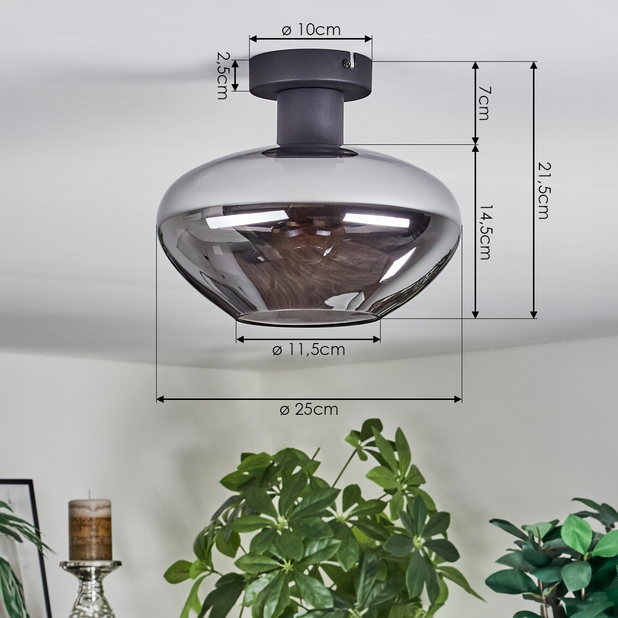 Eine moderne Deckenlampe mit Maßangaben. Darunter eine grüne Pflanze und ein Kerzenhalter. Die Lampe ist grau, die Decke weiß.