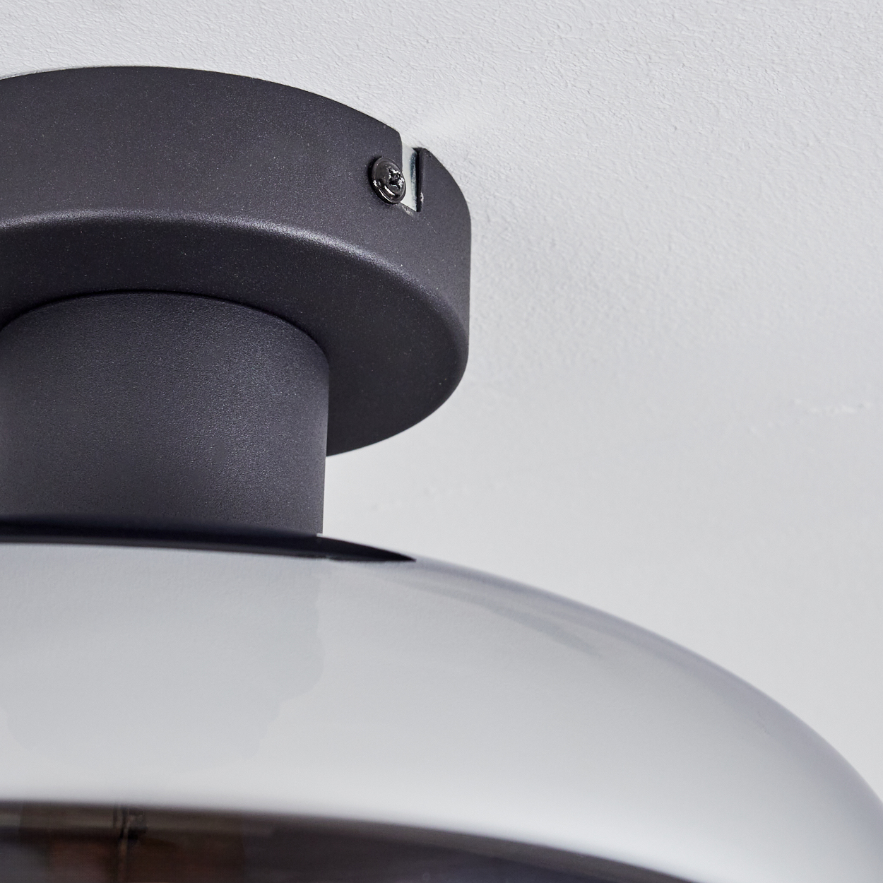 Nahaufnahme einer schwarzen Deckenleuchte vor einer weißen, strukturierten Decke. Die Lampe hat eine zylindrische Basis und einen gewölbten Schirm.