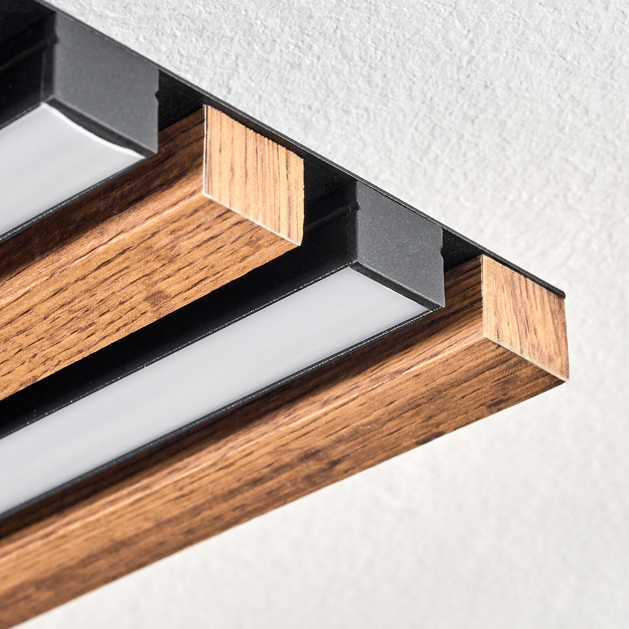 Nahaufnahme einer modernen Leuchte. Sie hat Holzbalken, schwarzes Metall und helle weiße LED-Leuchten. Der Hintergrund ist weiß.