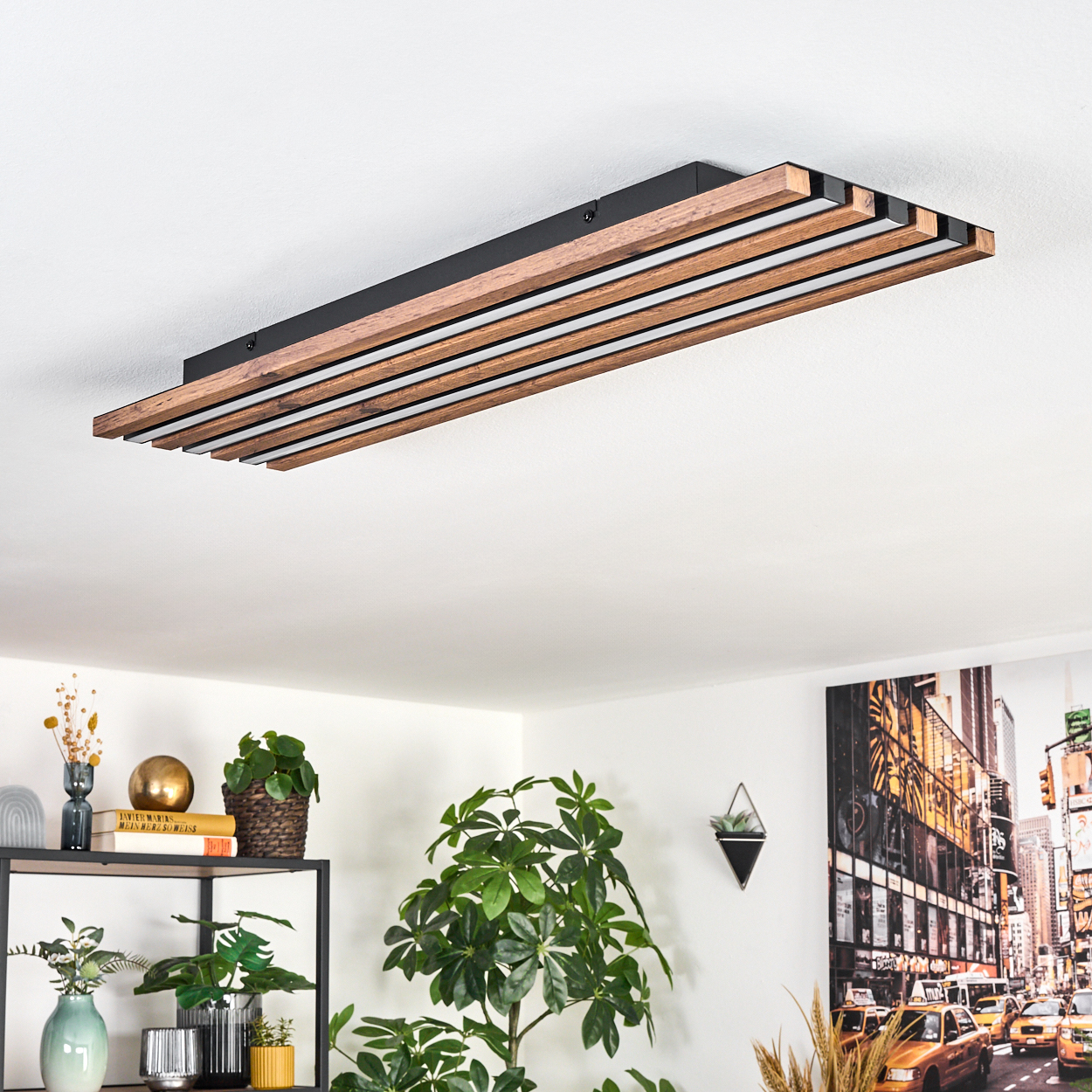 Eine moderne Deckenlampe mit Holzlatten und schwarzem Rahmen. Pflanzen und eine Stadtszene sind im Raum sichtbar.