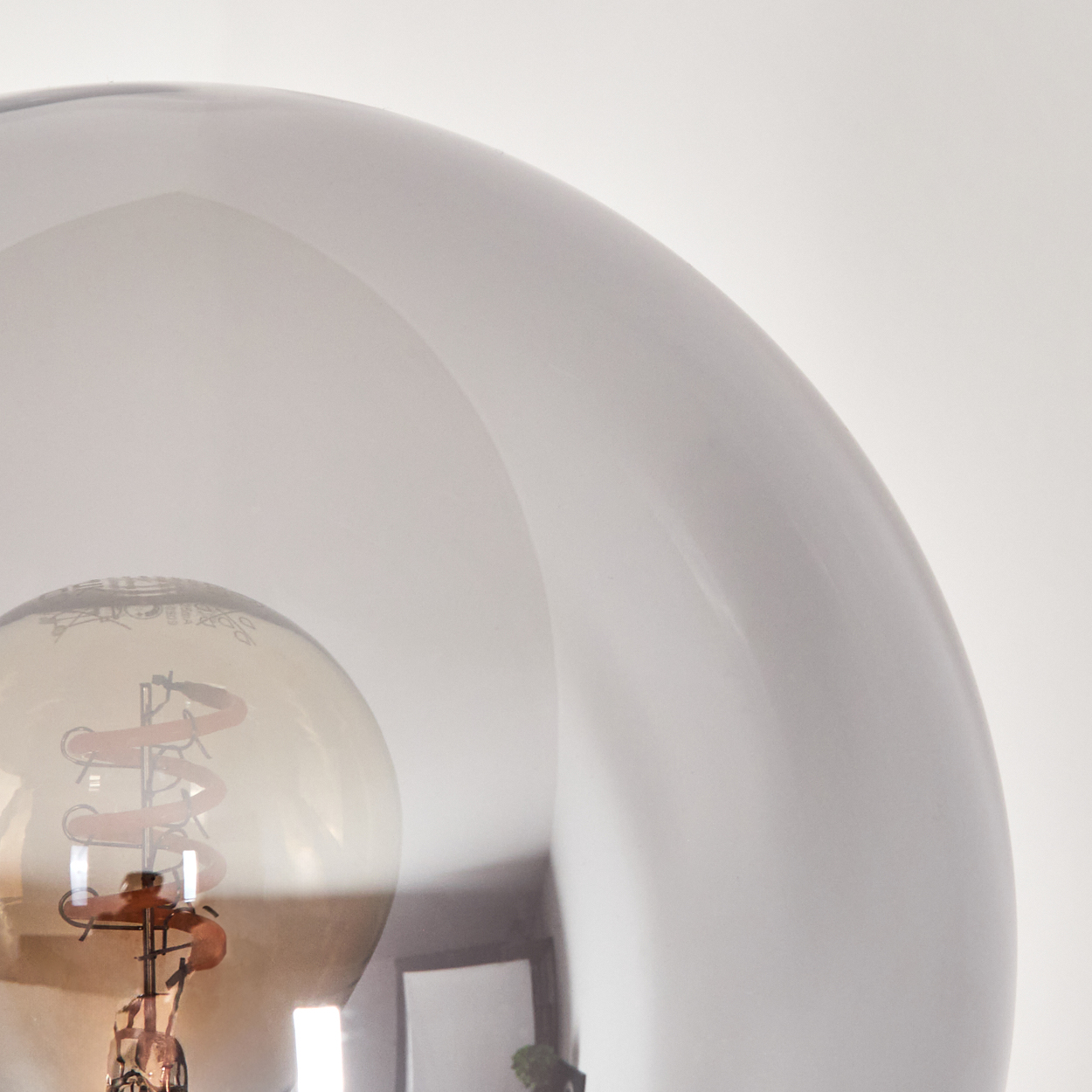 Nahaufnahme einer Glühbirne in einem transparenten, kugelförmigen Glas. Der Glühfaden der Glühbirne ist sichtbar. Der Hintergrund ist weiß.