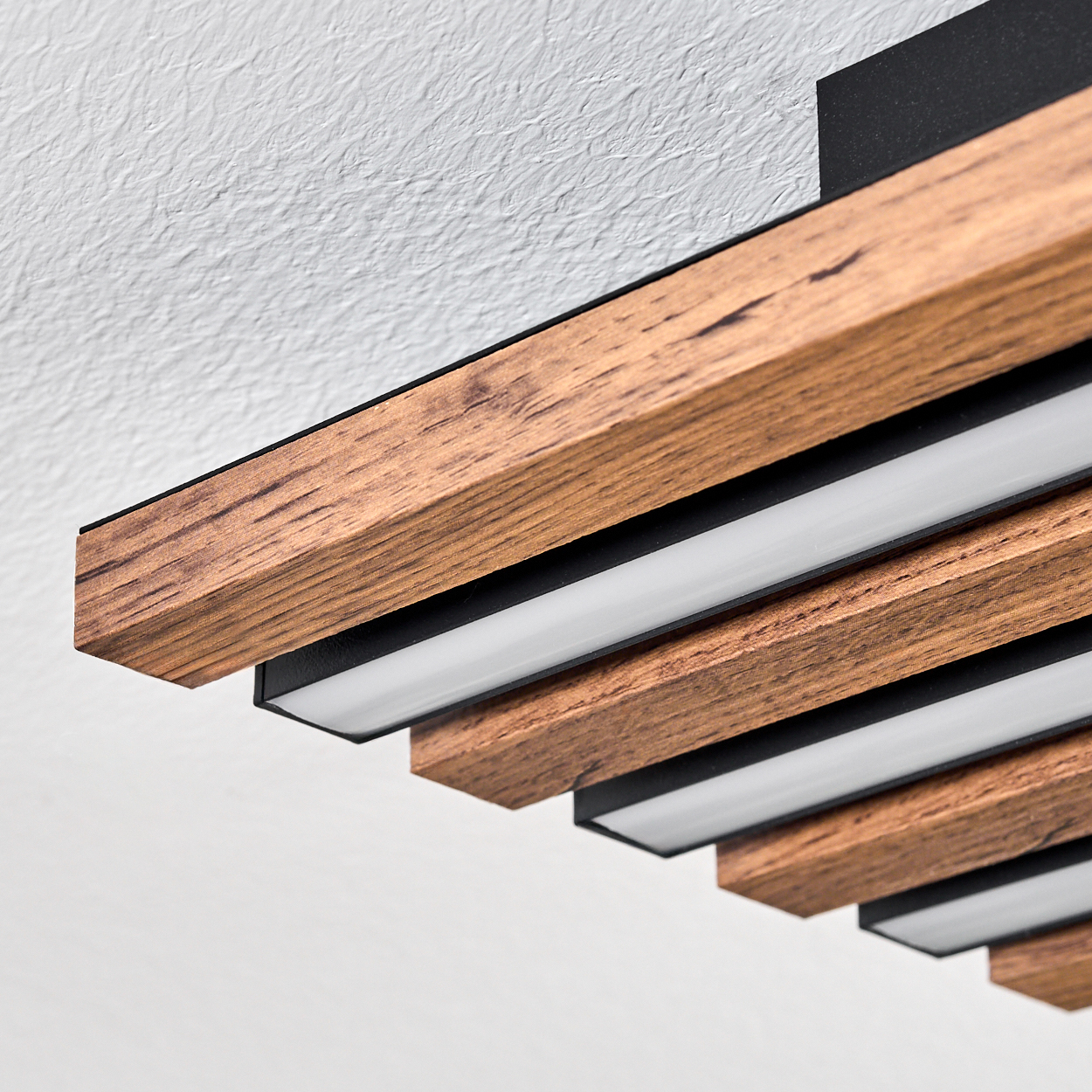 Nahaufnahme einer modernen Deckenleuchte aus Holz. Sie hat Holzbalken mit schwarzen Kanten und weißen Lichtstreifen.