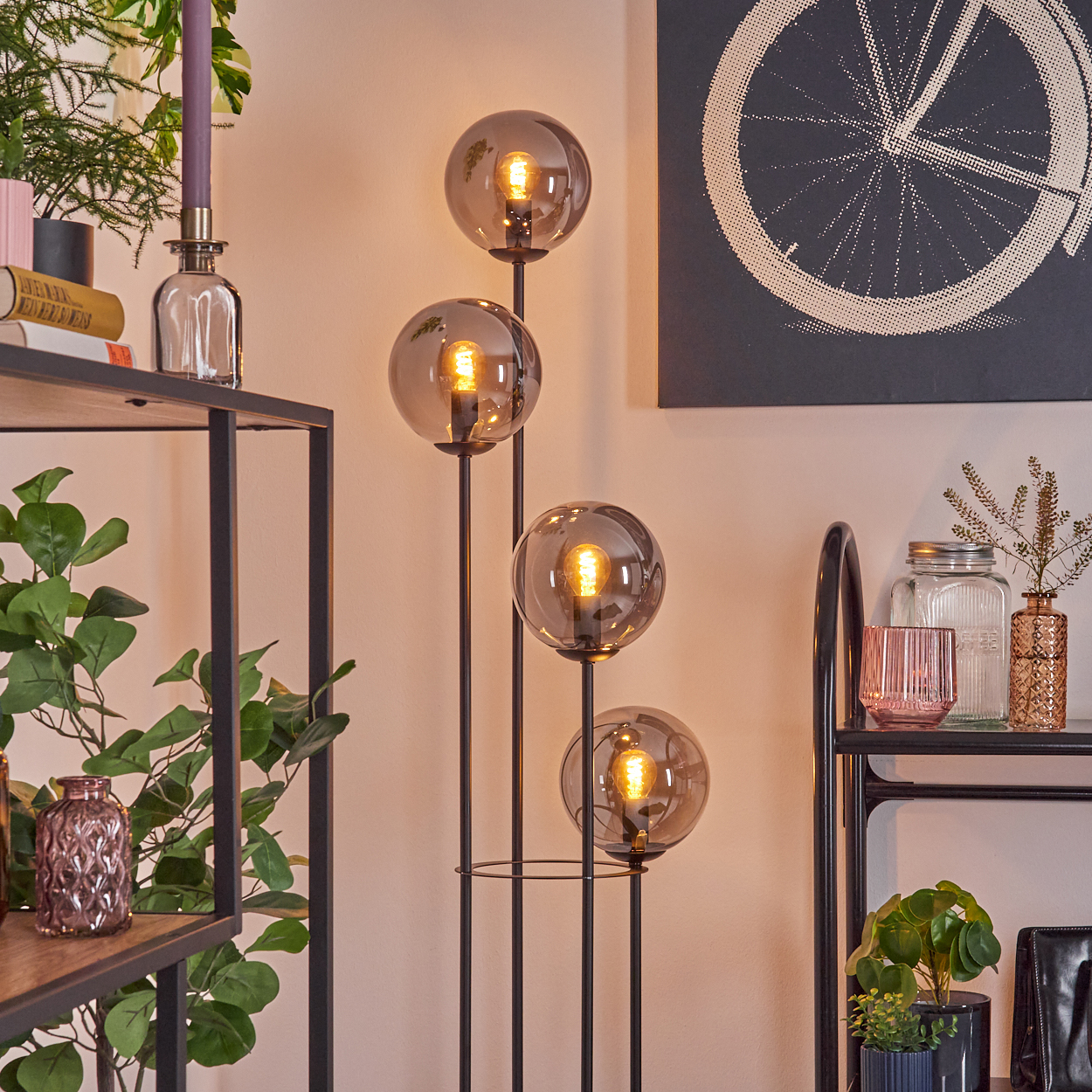 Ein modernes Wohnzimmer mit einem schwarzen Metallregal, einer Stehlampe mit vier Glaskugeln und Dekorationsgegenständen.