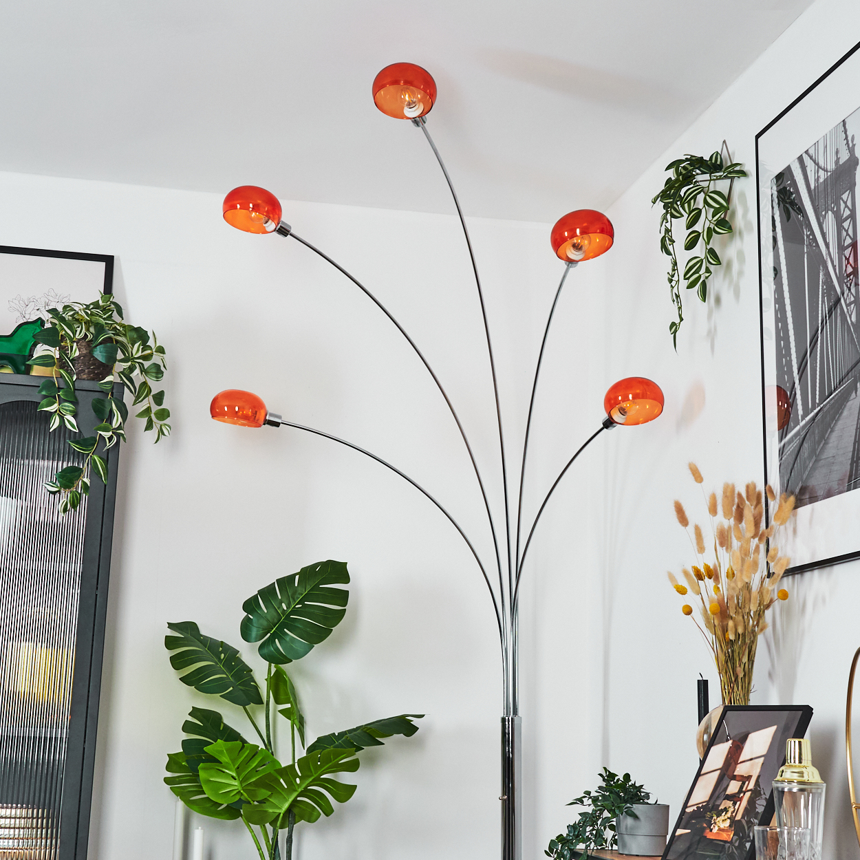 Ein modernes Wohnzimmer mit einer orangefarbenen Lampe, Pflanzen und gerahmten Kunstwerken. Die Lampe ist der Mittelpunkt.
