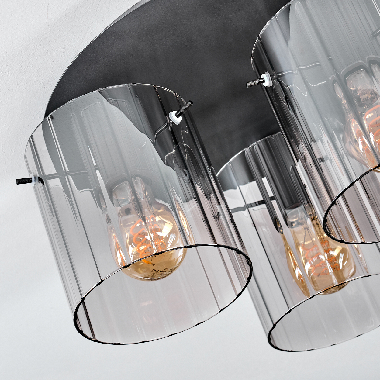 Nahaufnahme einer modernen Leuchte. Sie hat drei zylindrische Glasschirme mit freiliegenden Glühbirnen, die auf einer dunklen, kreisförmigen Basis montiert sind.