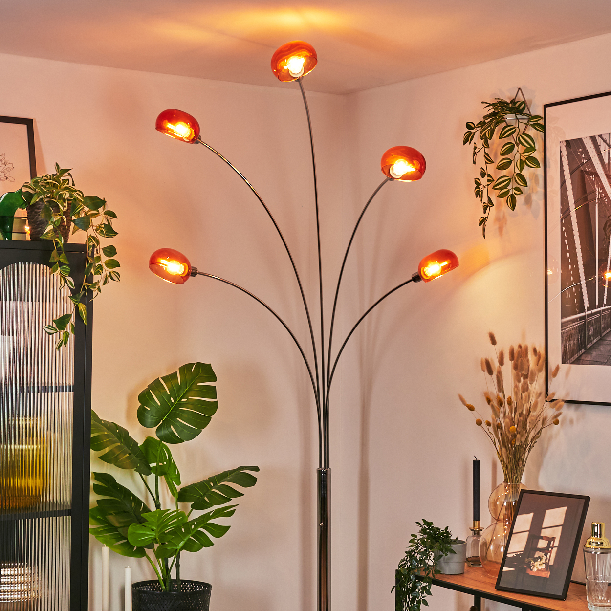 Ein modernes Wohnzimmer mit einer einzigartigen Stehlampe mit orangefarbenen Glasschirmen, umgeben von Pflanzen und Dekorationsartikeln.
