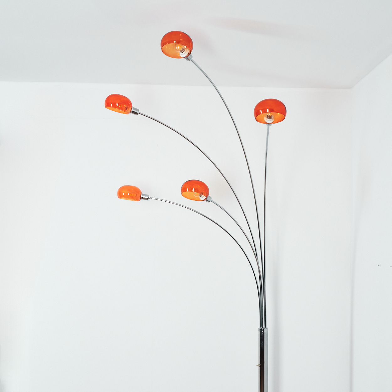 Eine moderne Stehlampe mit fünf orangefarbenen Glasschirmen. Der Sockel ist verchromt, die Arme sind nach oben gebogen. Der Hintergrund ist weiß.