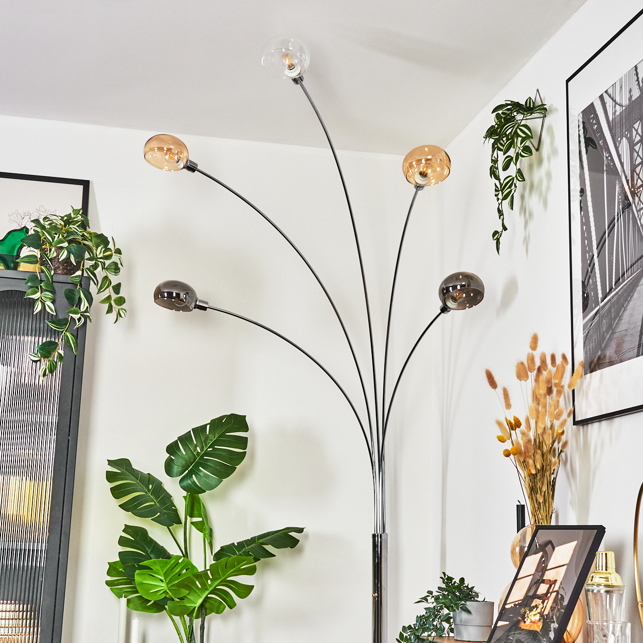 Ein modernes Wohnzimmer mit Stehlampe, Pflanzen und gerahmter Kunst. Die Lampe hat fünf Kugelleuchten. Pflanzen im Vordergrund.