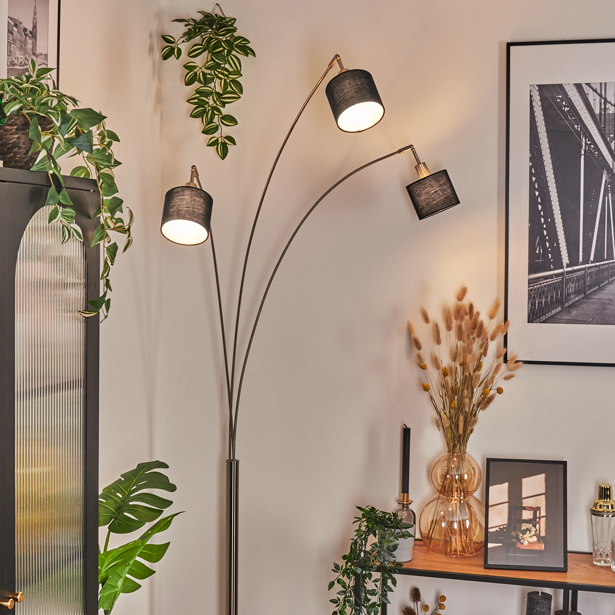Ein modernes Wohnzimmer mit Stehlampe, Pflanzen, gerahmtem Brückenfoto und Dekoration auf einem Holzregal.