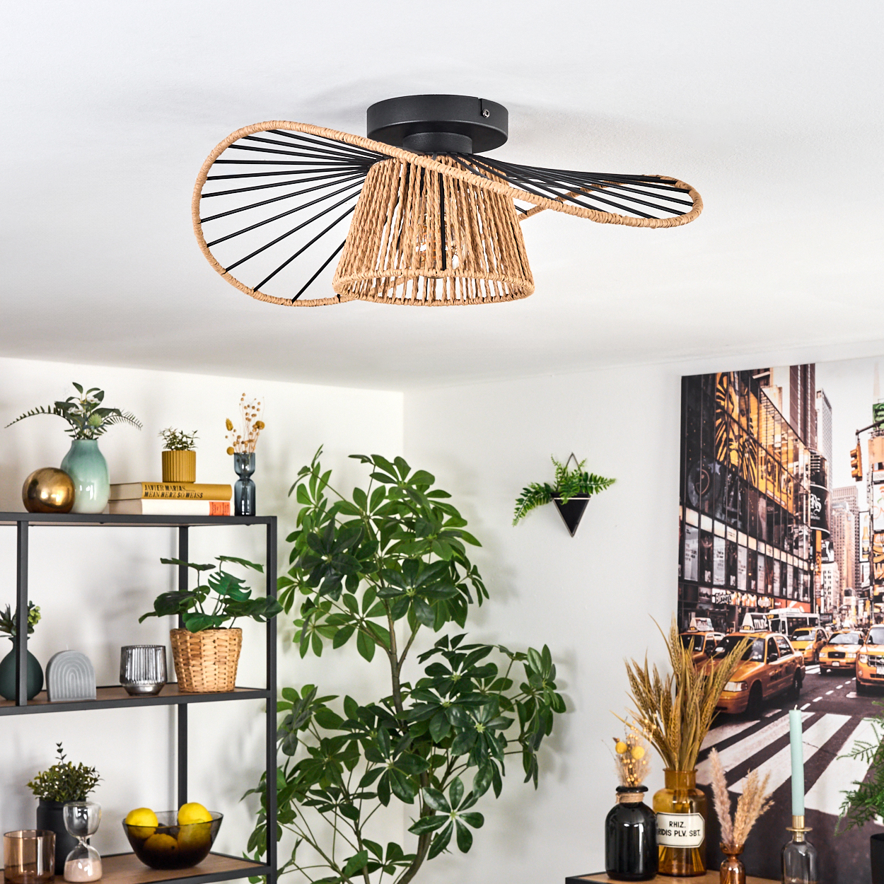 Ein gewebter Lampenschirm hängt von der Decke. Regale mit Vasen und Pflanzen sind sichtbar. Ein Gemälde von New York City ist an der Wand.
