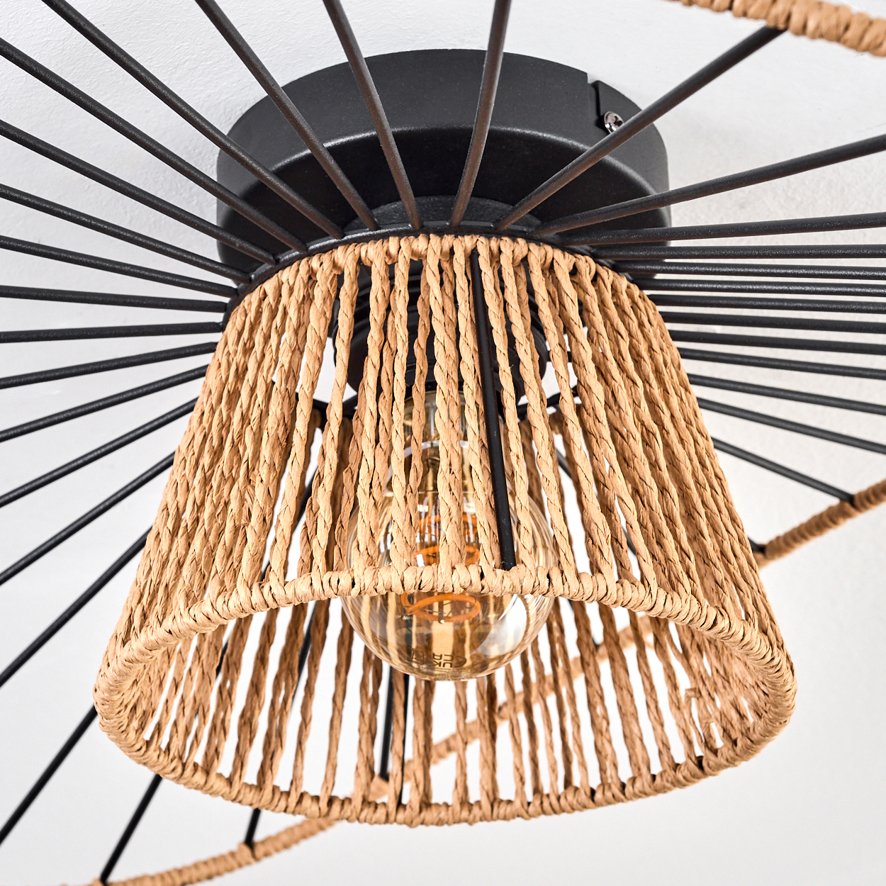 Eine moderne Deckenlampe mit gewebtem Lampenschirm und sichtbarer Glühbirne. Schwarzer Metallrahmen mit radialen Stäben.