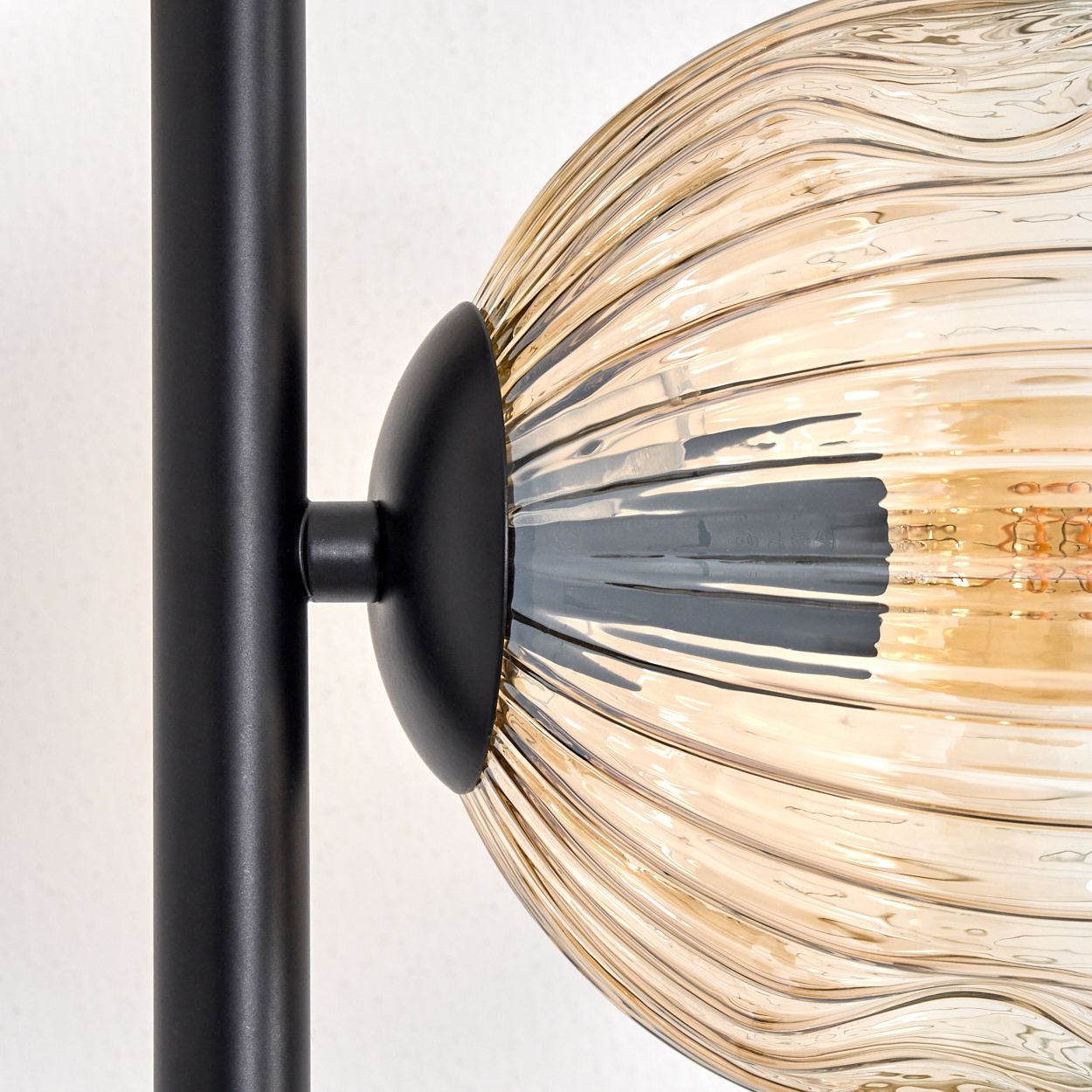 Nahaufnahme einer Lampe. Schwarzer Metallstiel trägt einen gerippten, bernsteinfarbenen Glasschirm. Licht scheint hindurch.