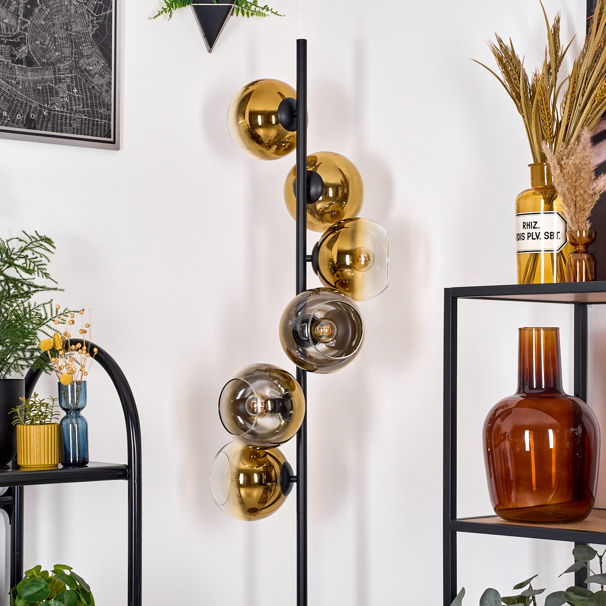 Eine moderne Stehlampe mit goldenen Glaskugeln. Regale mit Vasen, Pflanzen und einer Karte sind im Hintergrund sichtbar.