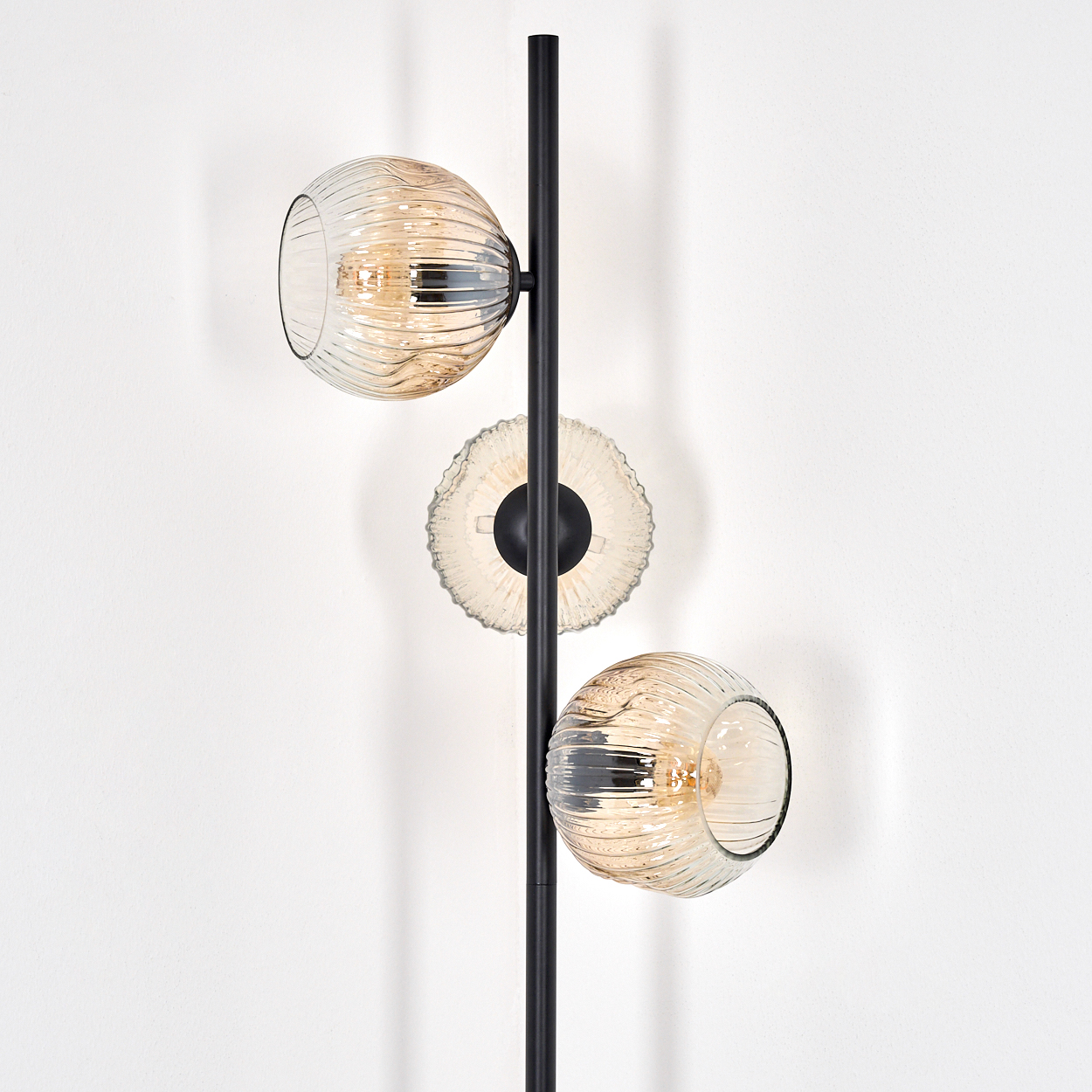 Eine moderne Stehlampe mit drei Glasschirmen. Die Schirme sind rund, mit gerippter Textur und warmer, bernsteinfarbener Farbe und einem schwarzen Stab.