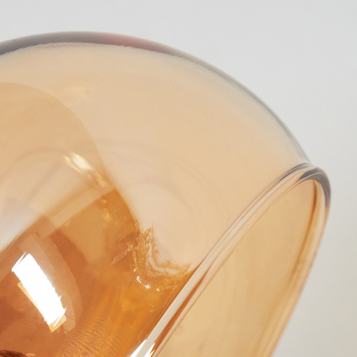Nahaufnahme eines transparenten, bernsteinfarbenen Glases. Das Licht reflektiert auf der gebogenen Oberfläche vor weißem Hintergrund.