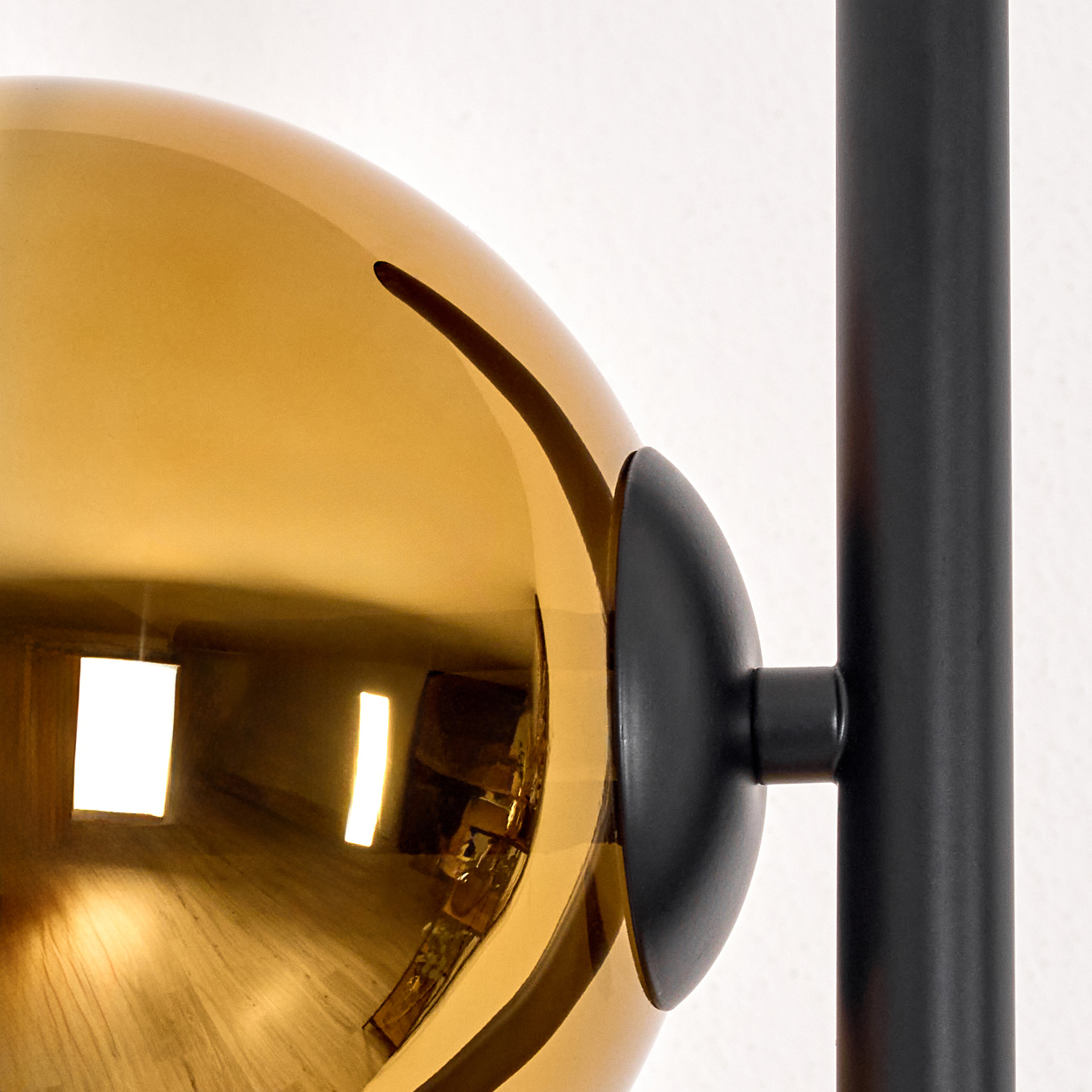 Nahaufnahme einer goldenen Glaskugel, die einen Raum reflektiert. Sie ist an einem schwarzen Metallrahmen vor weißem Hintergrund befestigt.