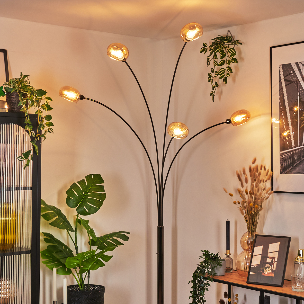 Ein modernes Wohnzimmer mit Stehlampe, Pflanzen und Bild. Die Lampe hat sechs Lichter. Pflanzen und Dekorationen sind sichtbar.