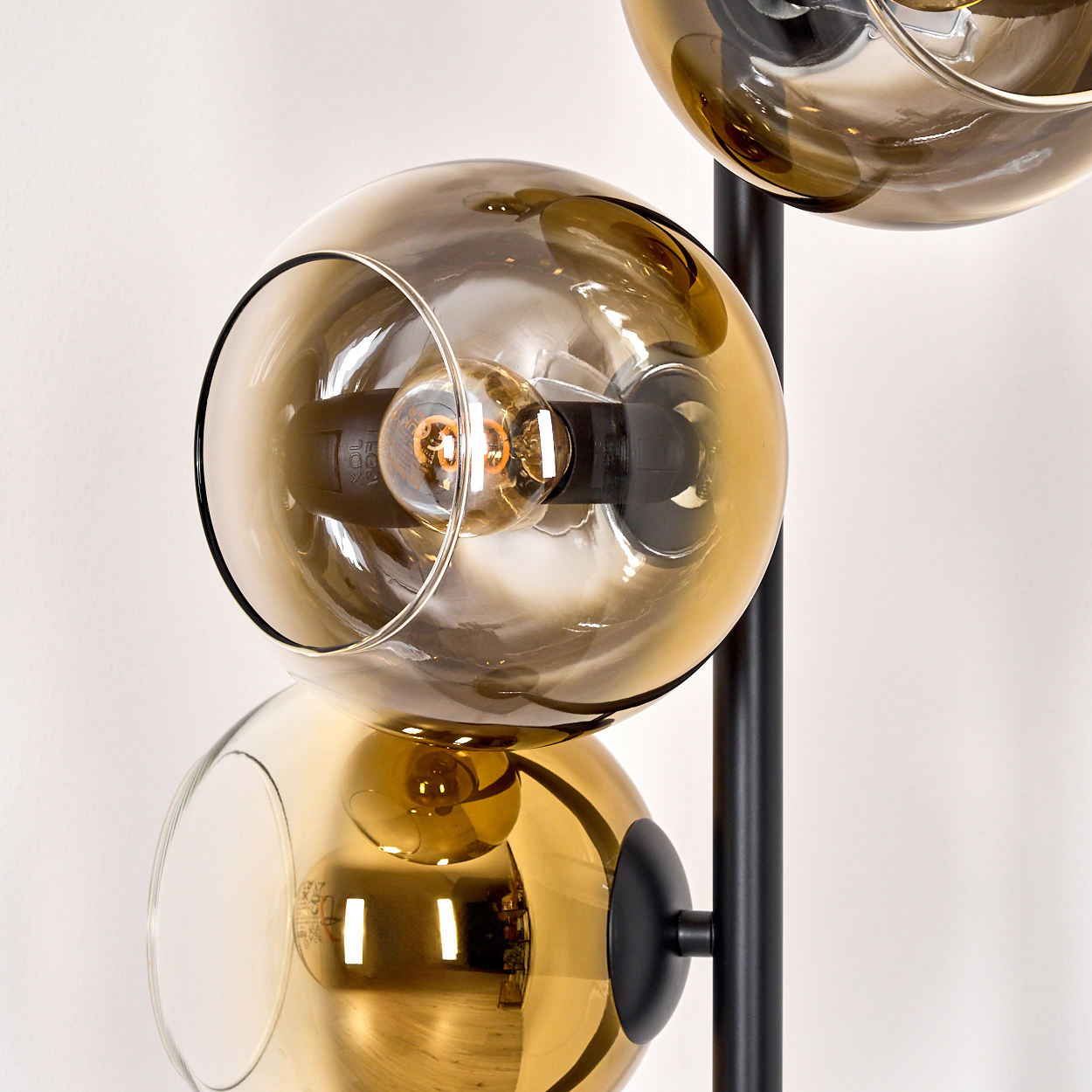Eine moderne Lampe mit drei kugelförmigen, bernsteinfarbenen Glasschirmen, die jeweils eine Glühbirne enthalten. Sie steht vor weißem Hintergrund.
