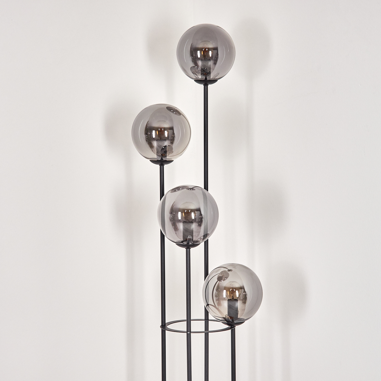 Eine moderne Stehlampe mit vier grauen Glaskugelschirmen. Die Lampe hat einen schwarzen Metallrahmen vor einer weißen Wand.