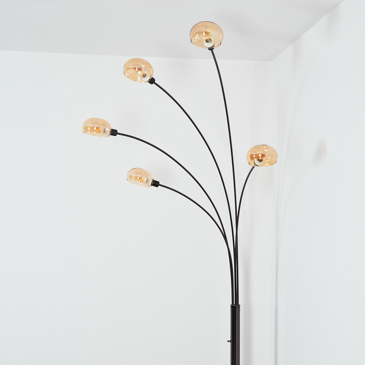 Eine moderne Stehlampe mit fünf bernsteinfarbenen Kugelleuchten an schwarzen Stielen vor einer weißen Wand.