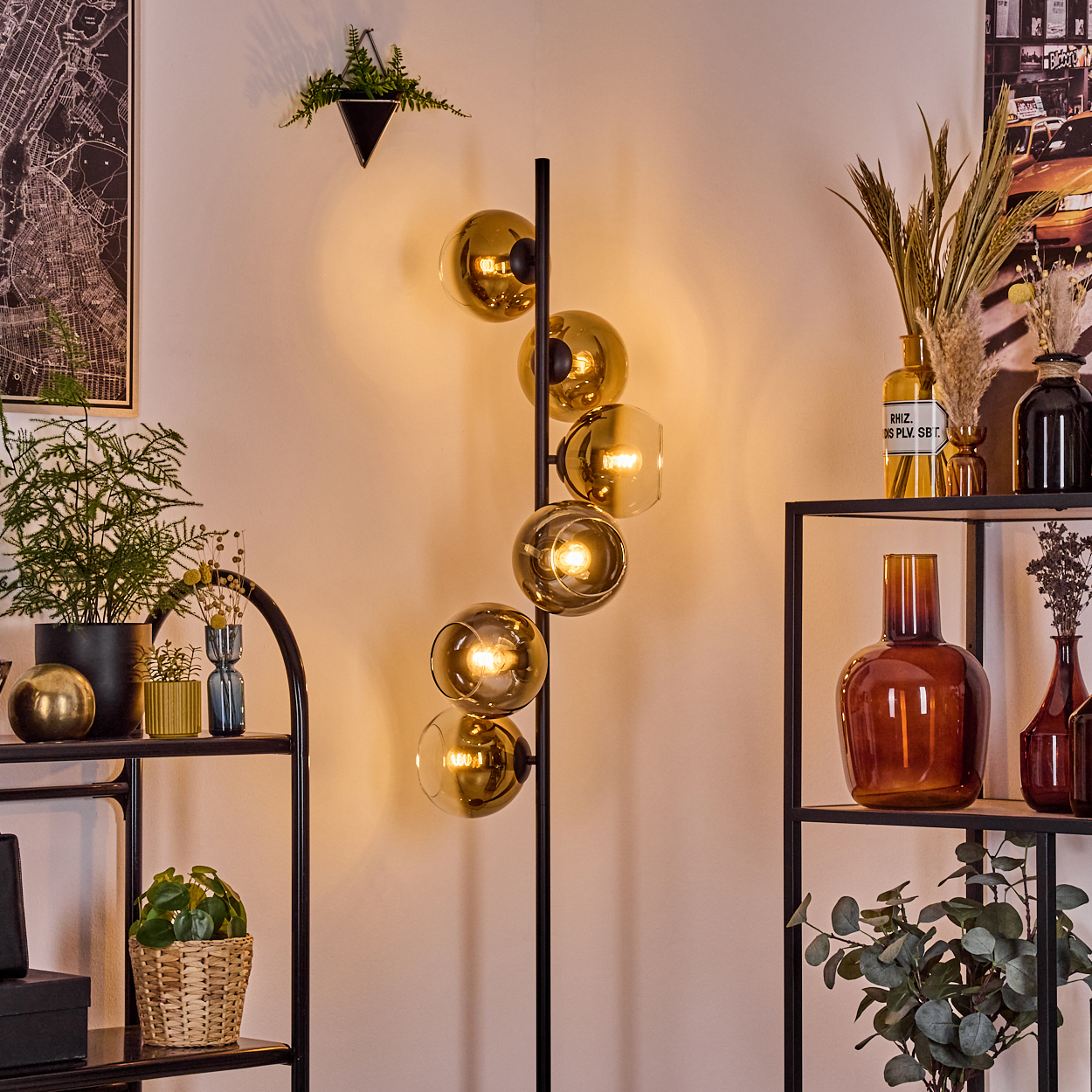 Ein modernes Wohnzimmer mit einer schwarzen Stehlampe mit Glaskugeln. Regale mit Pflanzen und Vasen befinden sich an den Seiten.