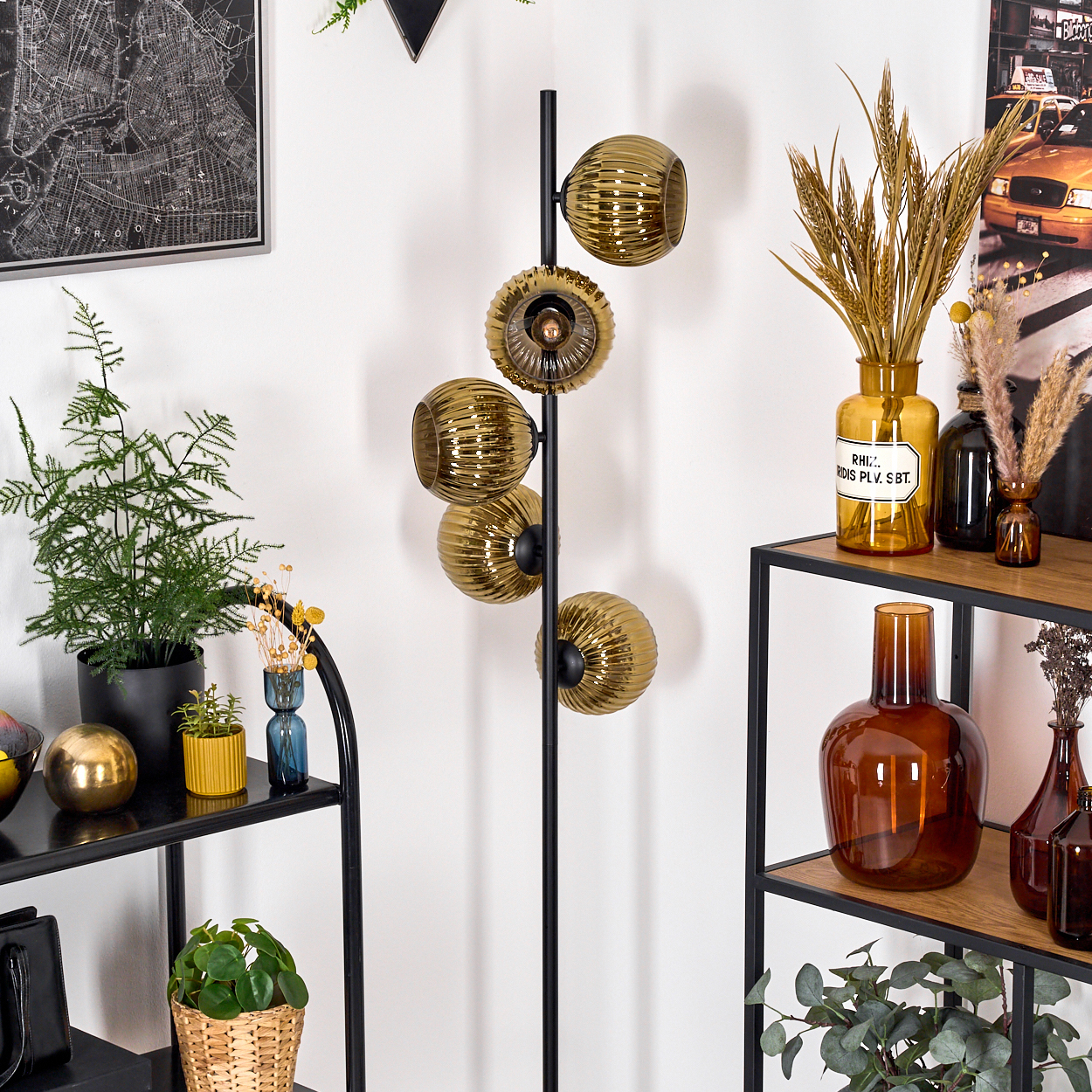 Ein Raum mit schwarzen Regalen, Pflanzen und dekorativen Vasen. In der Mitte steht eine schwarze Stehlampe mit goldenen Kugeln.