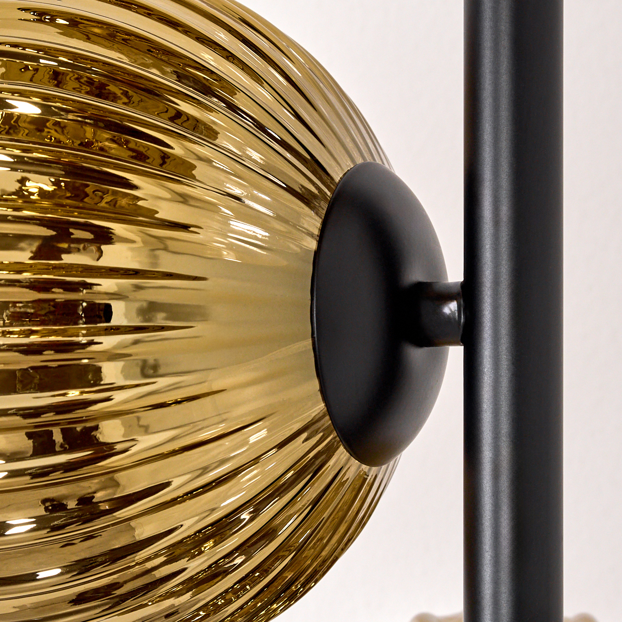 Nahaufnahme einer Lampe. Eine gerippte, goldene Glaskugel ist mit einem schwarzen Metallpfosten verbunden.