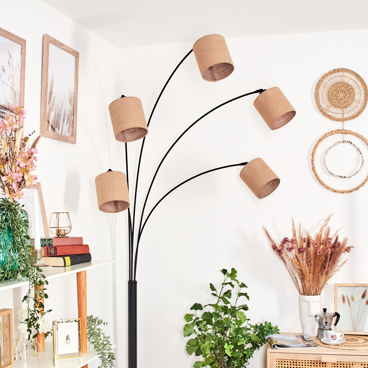 Ein modernes Wohnzimmer mit Stehlampe, Pflanzen und dekorativen Gegenständen. Die Lampe hat fünf beige Schirme. Weitere Dekorationen sind Bilder und Bücher.