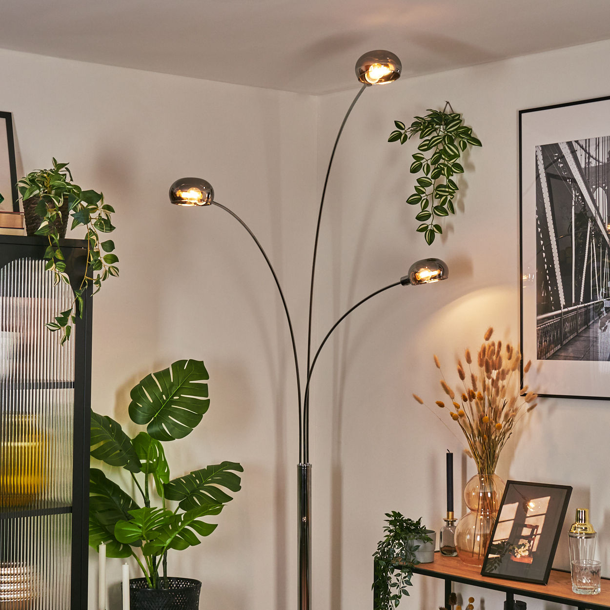 Ein modernes Wohnzimmer mit Stehlampe, Pflanzen und gerahmter Kunst. Die Lampe hat drei Lichter. Pflanzen sind verschiedene Arten.