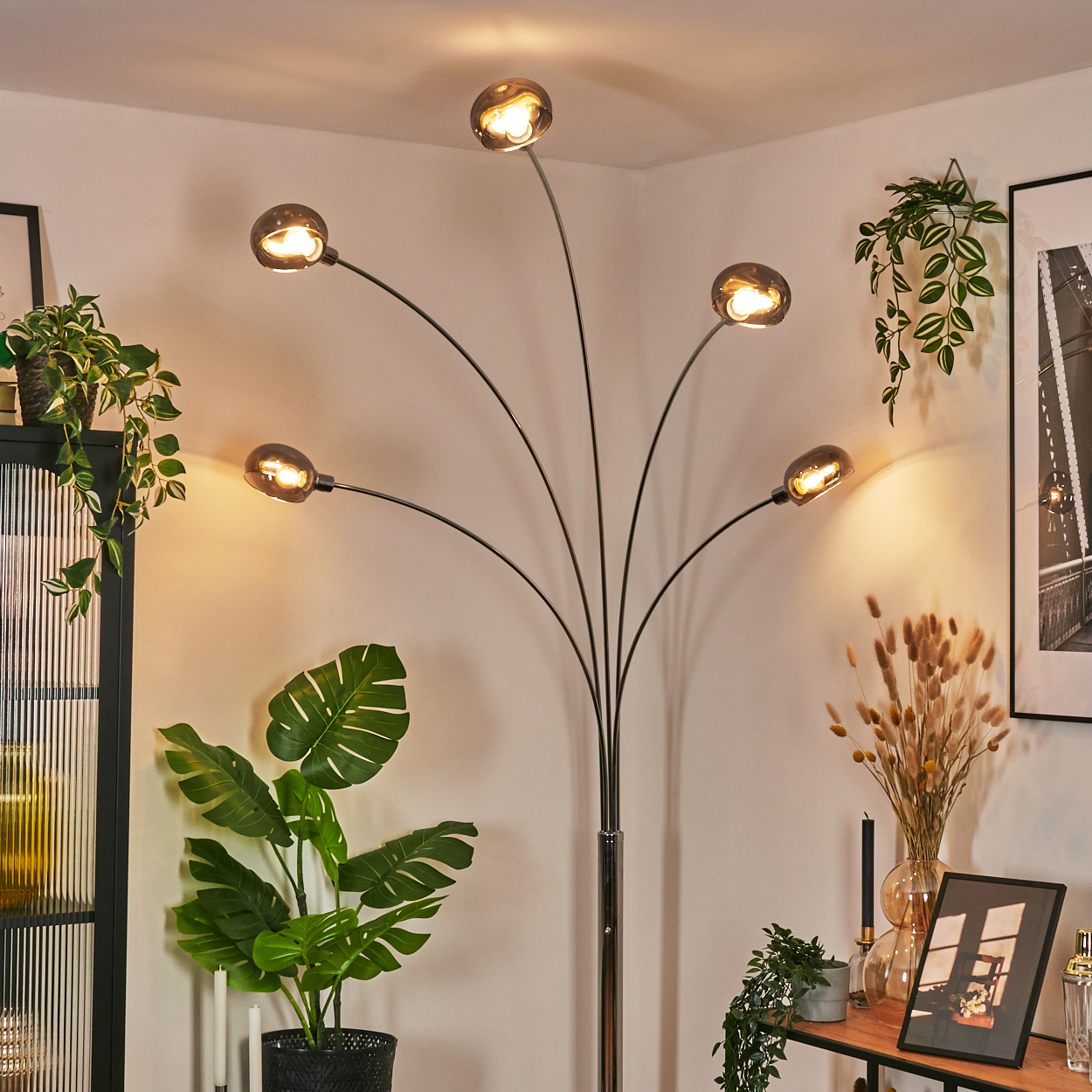 Ein modernes Wohnzimmer mit Stehlampe, Pflanzen und Dekoration. Die Lampe hat fünf Lichter. Pflanzen und Bilder an der Wand.