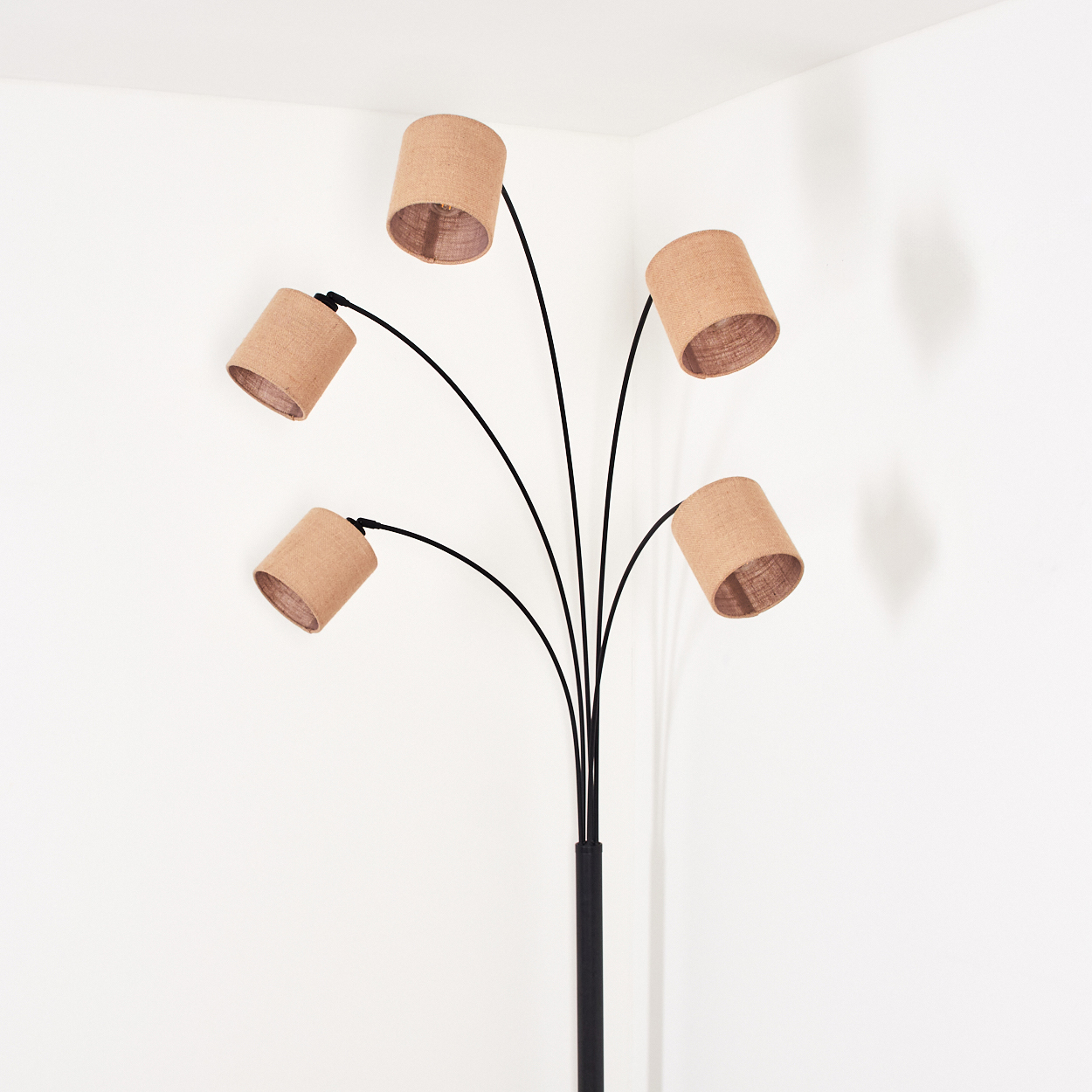 Eine moderne Stehlampe mit fünf beigefarbenen Lampenschirmen, schwarzen Stielen und einem schwarzen Fuß, vor einer weißen Wand in einer Ecke.