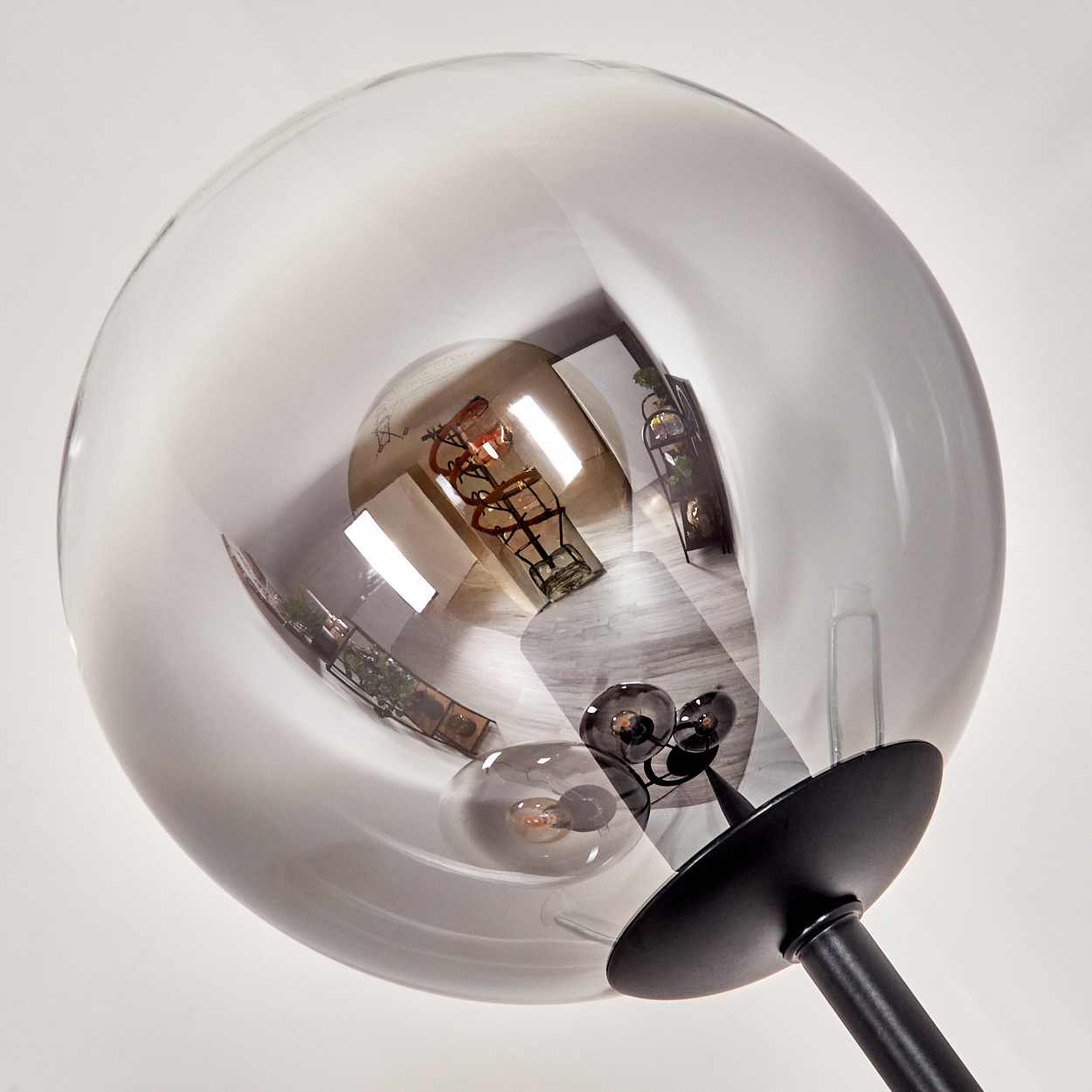 Eine moderne Lampe mit einem großen, transparenten Globus. Im Inneren ist eine Glühbirne sichtbar. Die Lampe hat einen schwarzen Fuß.