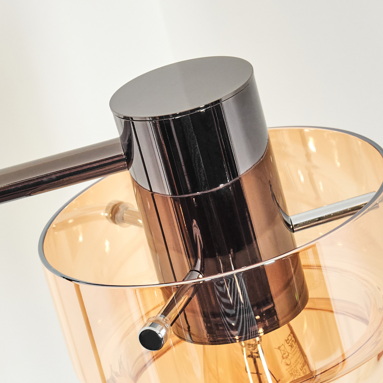Eine moderne Lampe mit Chrom- und Kupferausführung. Der Schirm ist aus bernsteinfarbenem Glas, die Glühbirne ist sichtbar. Der Hintergrund ist weiß.