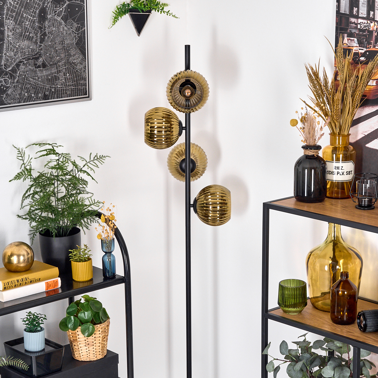Eine Zimmerecke mit einem schwarzen Metallregal. Eine Stehlampe mit goldenen Kugeln, Pflanzen und dekorativen Flaschen sind vorhanden.