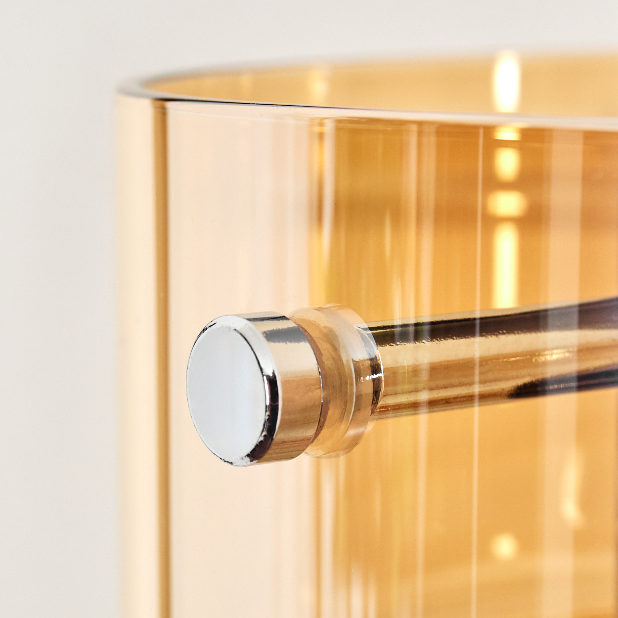 Nahaufnahme eines goldenen Glases mit silbernem Griff. Das Glas ist transparent und reflektiert Licht. Der Hintergrund ist beige.